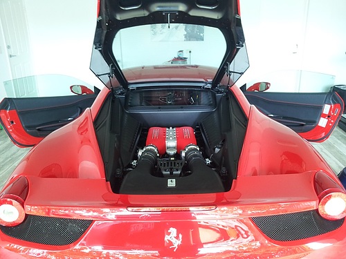 Red Ferrari with rear hatch open revealing its mid-mounted red engine, both doors ajar in a showroom.