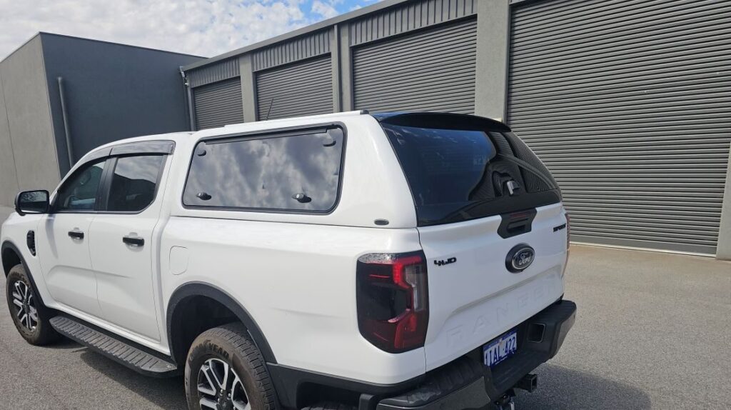 White Ford Ranger dual-cab ute with matching canopy and tinted rear window parked in front of grey metal roller doors.
