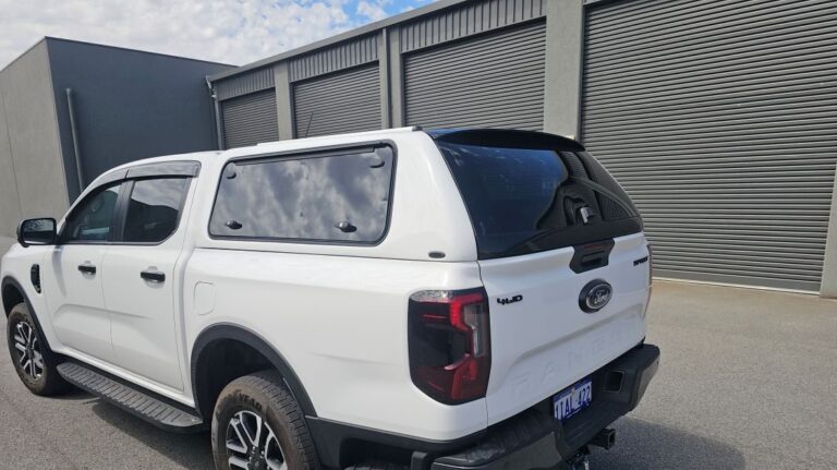 White Ford Ranger dual-cab ute with matching canopy and tinted rear window parked in front of grey metal roller doors.