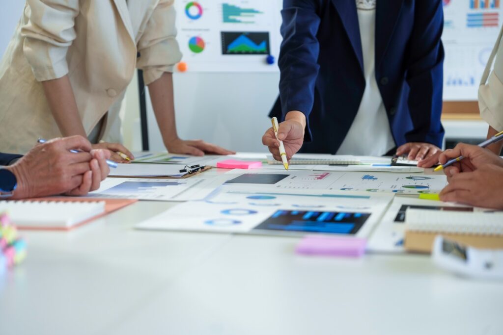 Team gathered around a table reviewing printed charts and graphs, one person pointing with a pen.