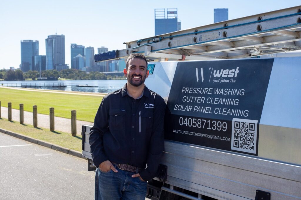 Smiling man leaning on a work truck with West Coast Exterior sign listing pressure washing, gutter and solar cleaning.