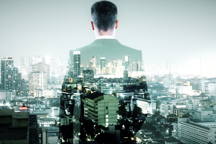 Man in a suit seen from behind overlaid with a glowing city skyline in a double-exposure effect.