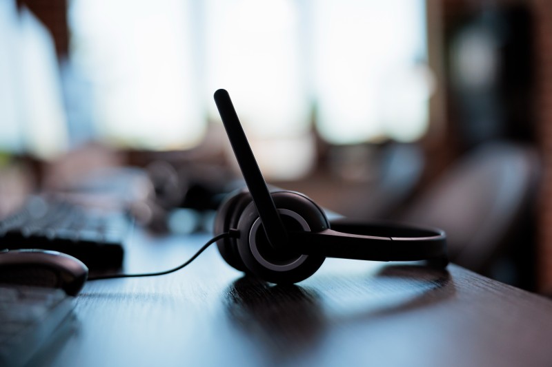 Black over-ear headset with a boom microphone resting on a wooden desk in a blurred office background.