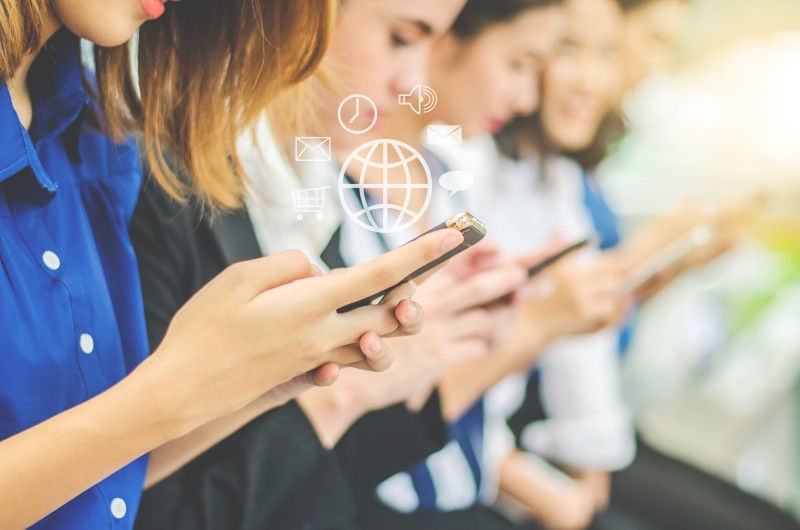 Several people in a line using smartphones, with translucent globe and app icons hovering over the devices.