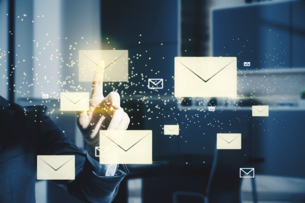 Hand in a suit tapping glowing virtual email envelopes floating amid digital particles in an office