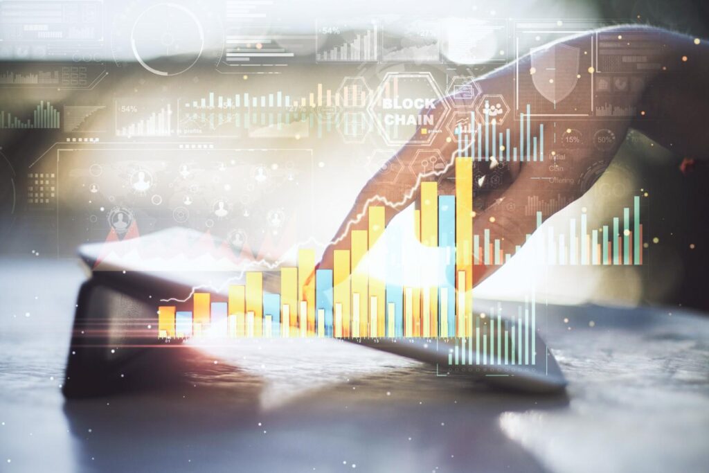 Hand tapping a tablet overlaid with translucent colourful bar charts and blockchain analytics graphics