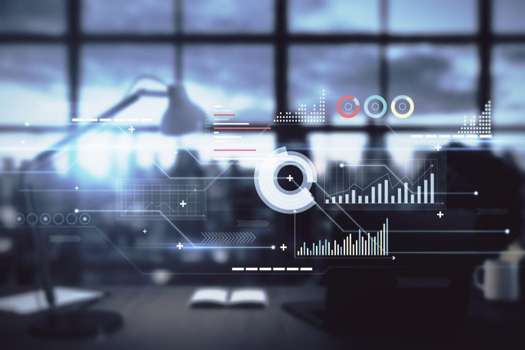 Blurred office desk and window with translucent digital data overlays showing charts, graphs and a circular infographic.