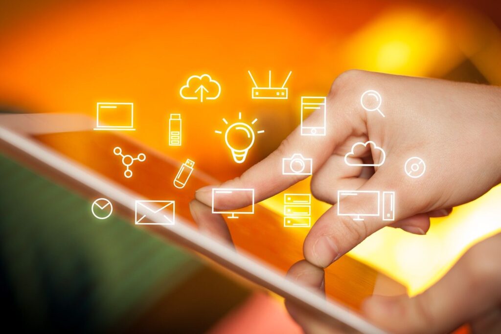 Finger tapping a tablet with floating white icons (cloud, lightbulb, email, camera) on a warm orange background.