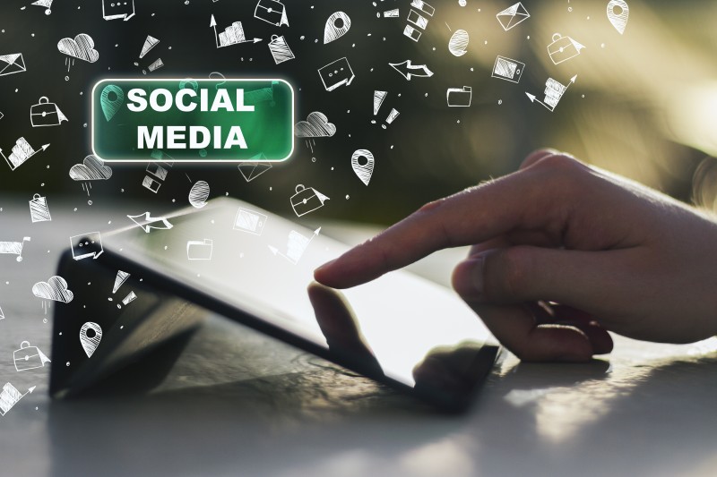 Hand tapping a tablet screen with floating social media icons and a green badge reading SOCIAL MEDIA.