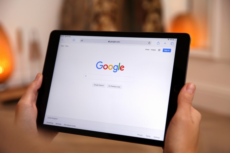 Hands holding a tablet displaying the Google search homepage with an empty search bar
