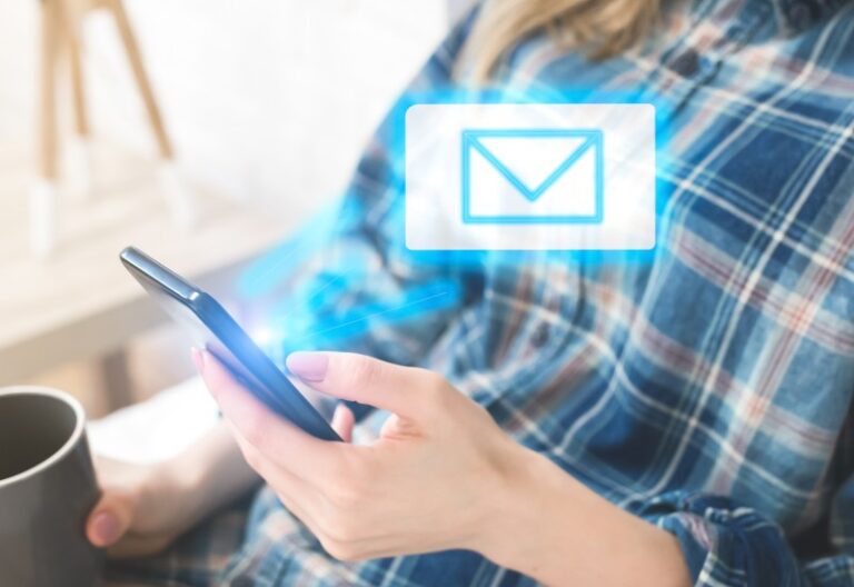 Person in a blue plaid shirt holding a smartphone and coffee mug with a glowing holographic email envelope above the phone.
